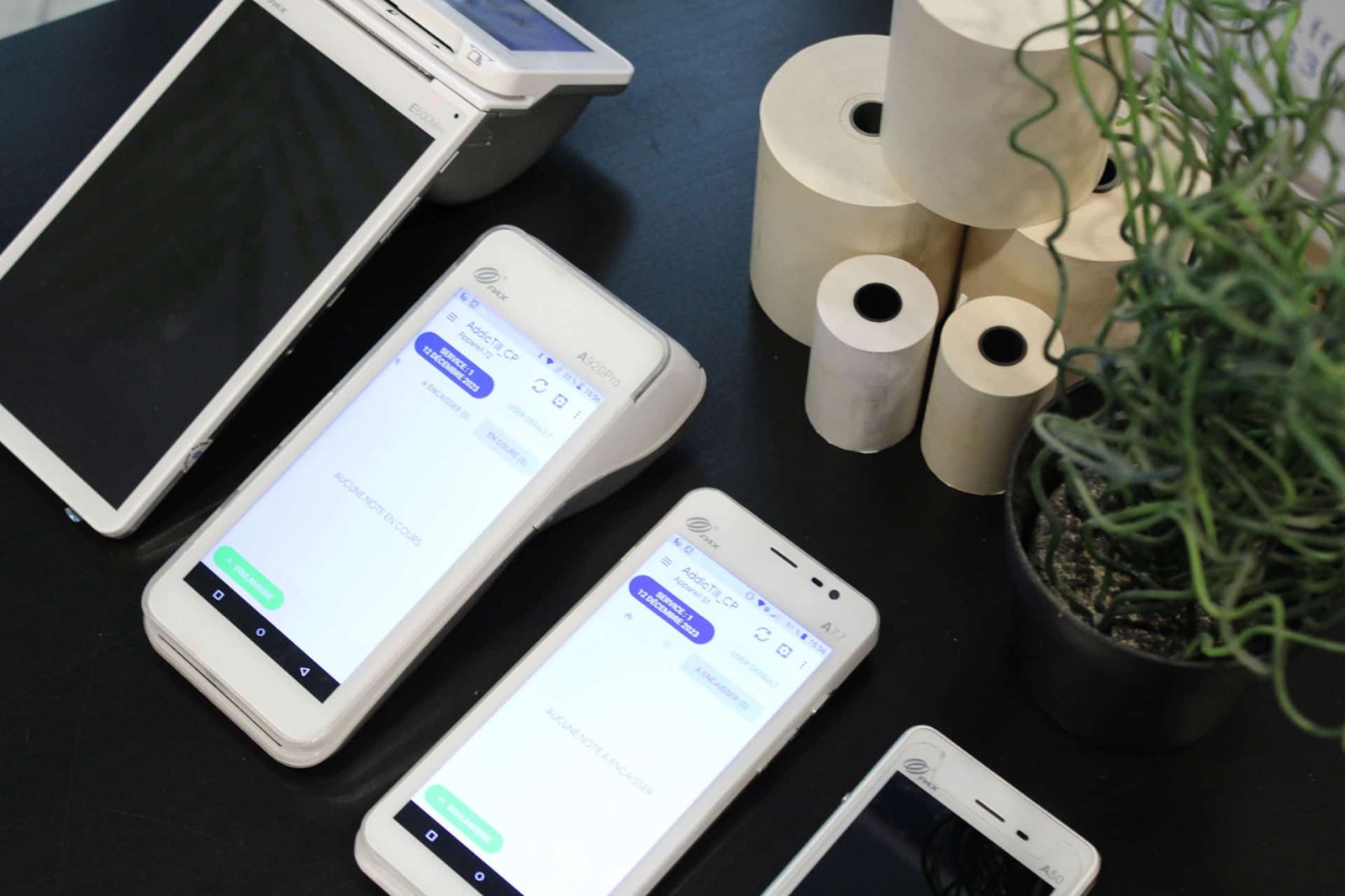 Plusieurs terminaux de paiement Android posés sur une table, à côté de rouleaux de papier thermique